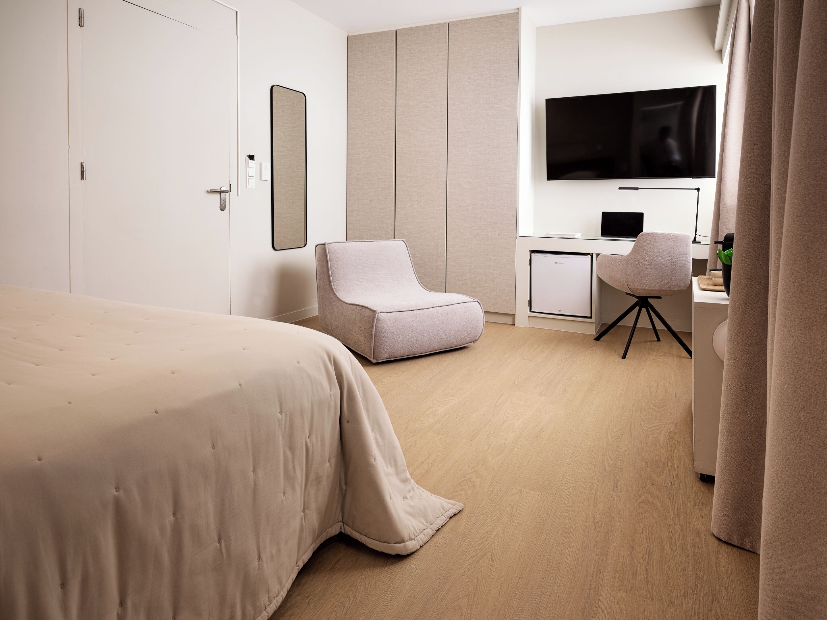 A hotel room with a bed, a desk with a computer, a chair, and a TV.