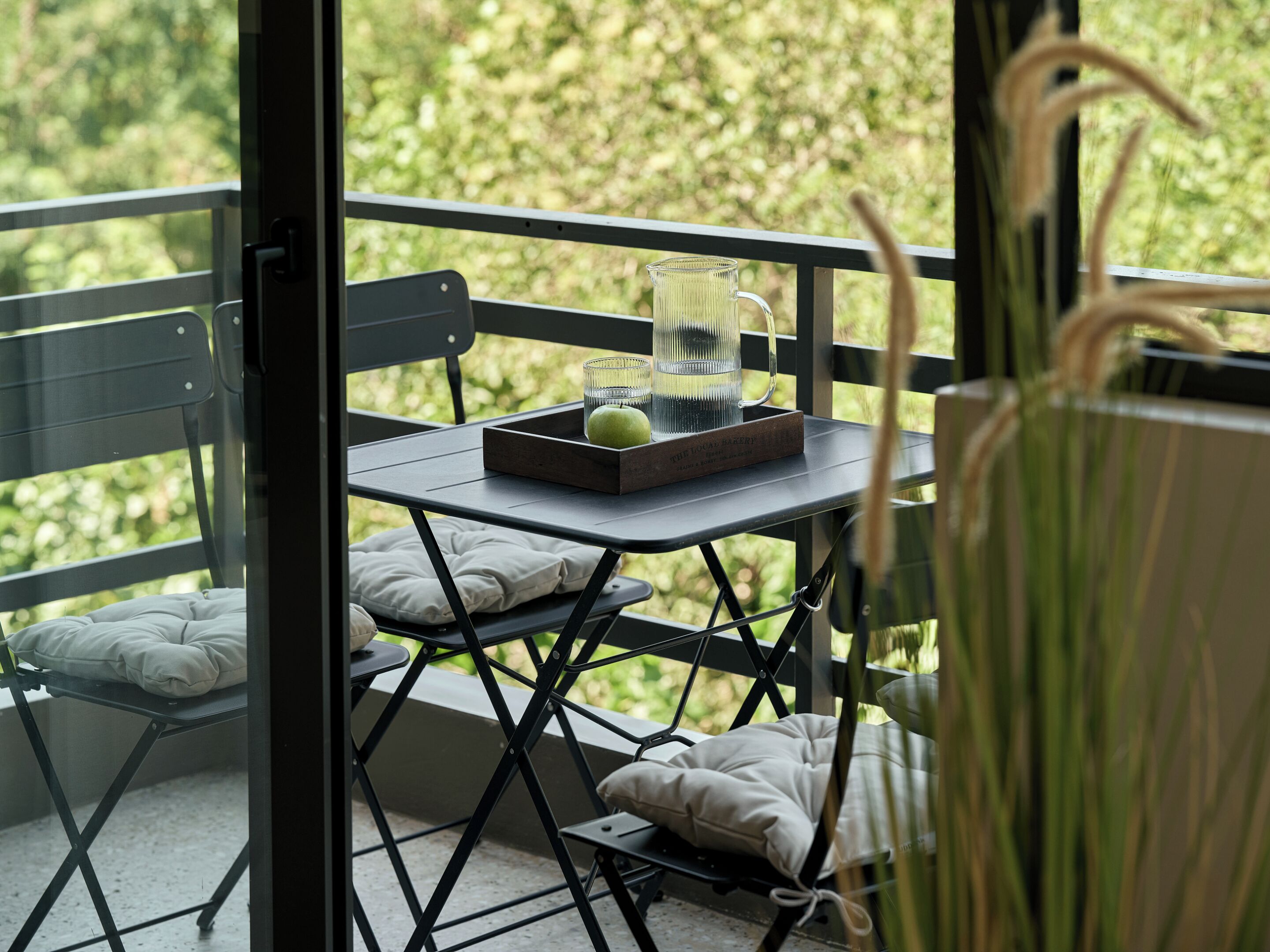 A balcony with a table, a chair, and a view of greenery.