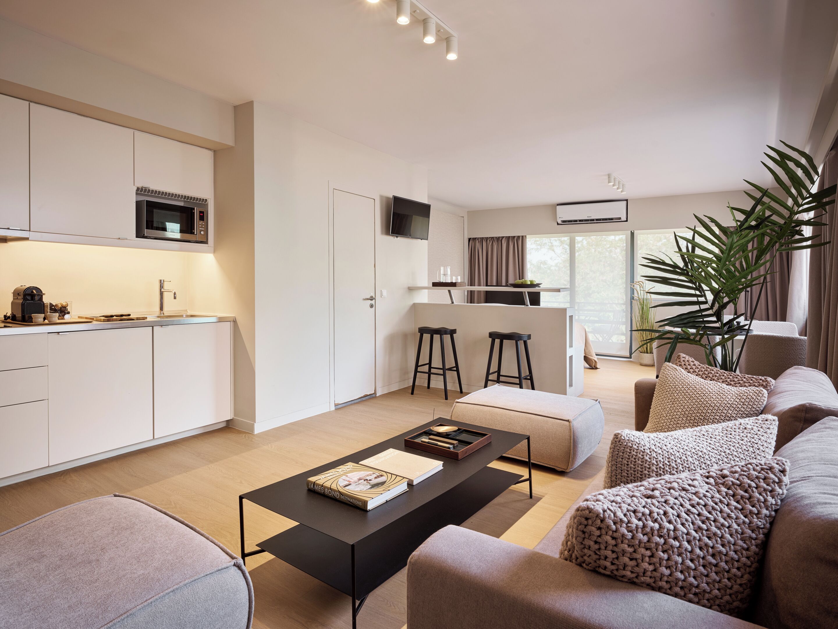 A modern living room with a coffee table, sofa, and a kitchen area with a microwave and bar stools.