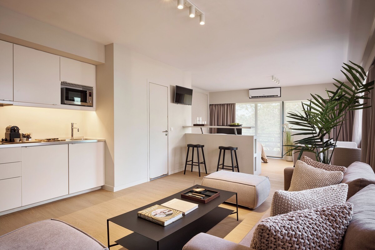 Una sala de estar moderna con una mesa de centro, sofá y una cocina con microondas y taburetes de bar.