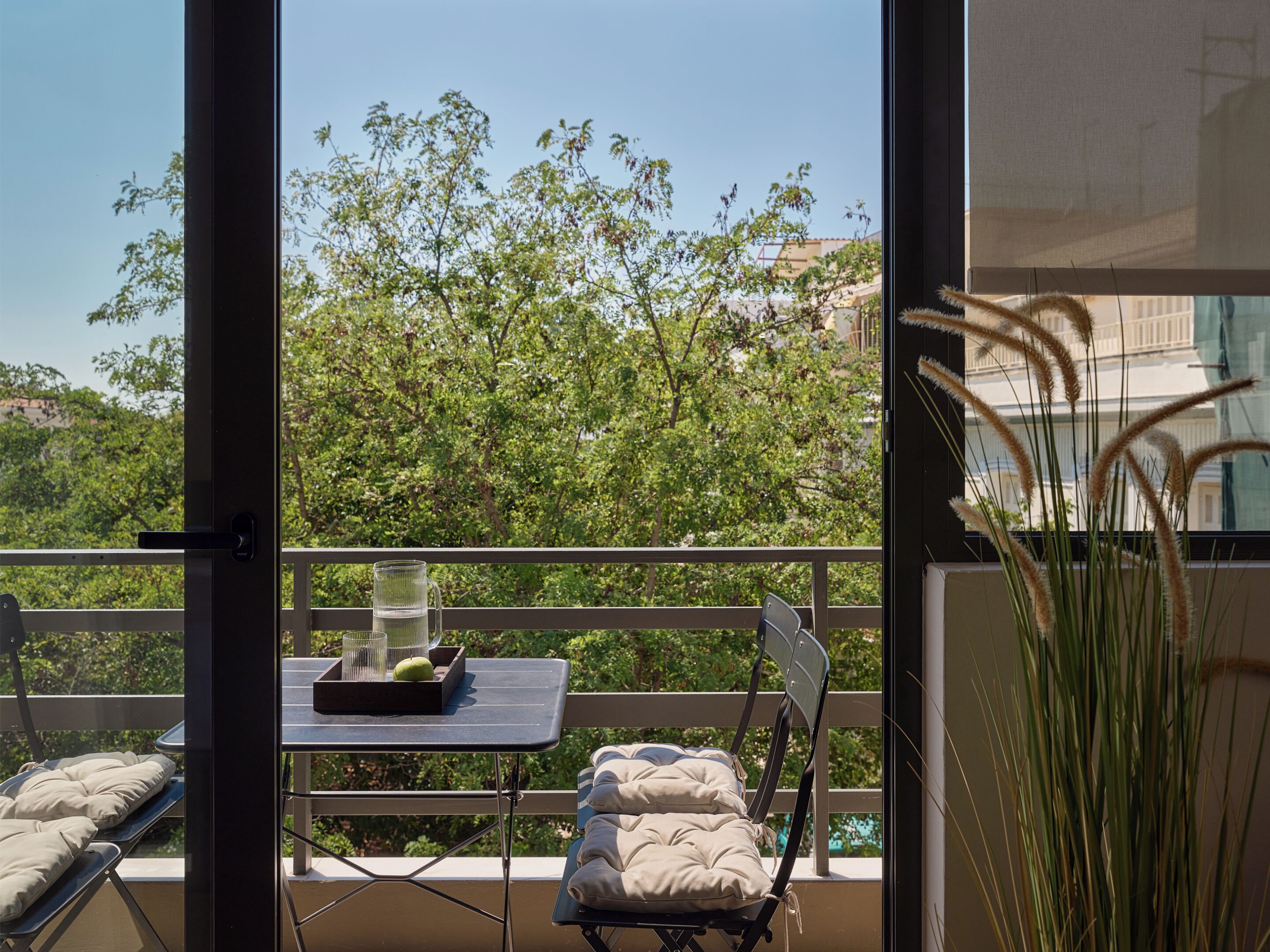 A balcony with a table, chairs, and a view of trees and buildings.