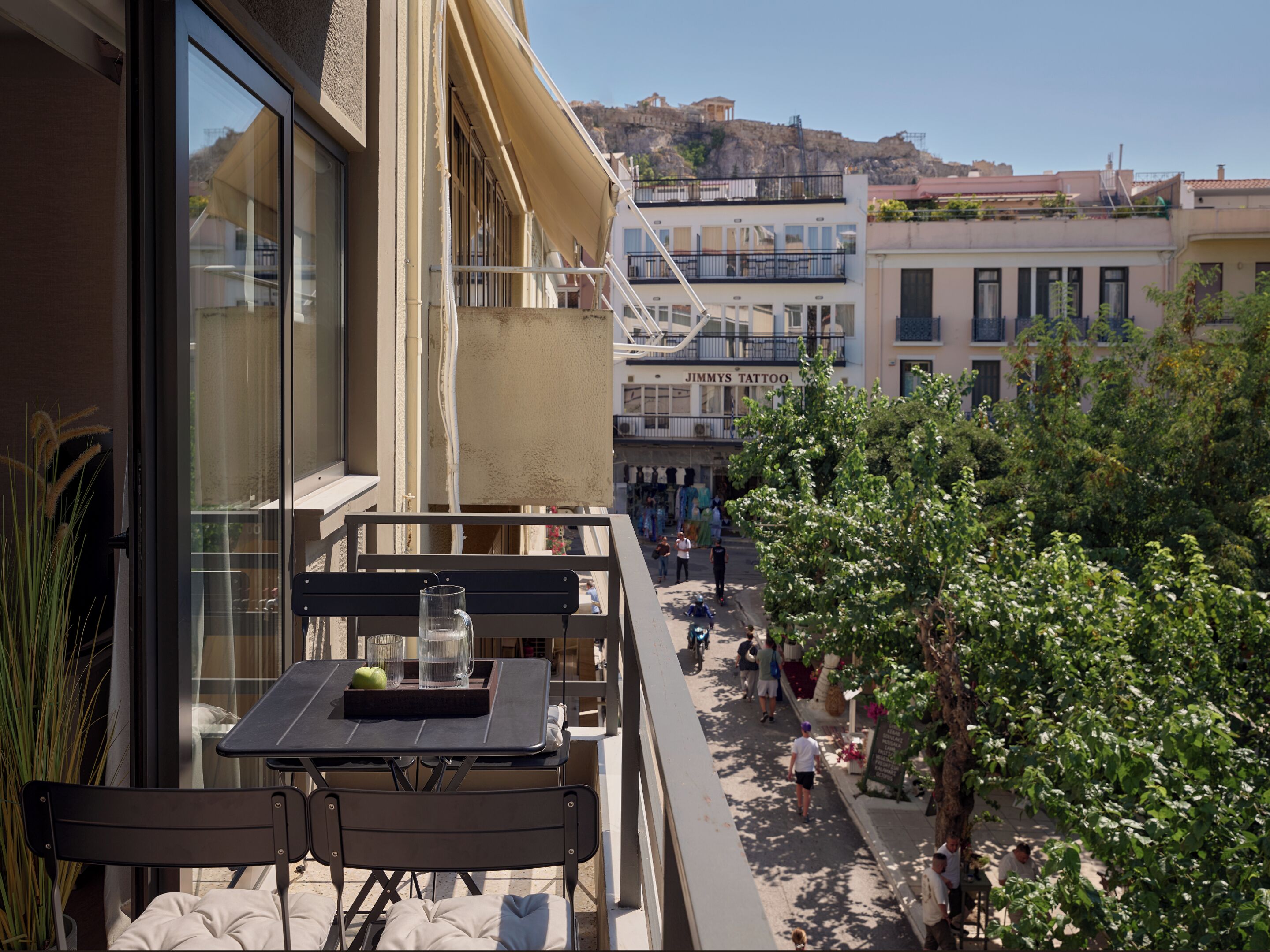 A balcony with a table and chairs, overlooking a street with pedestrians and buildings.