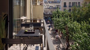 A balcony with a table and chairs, overlooking a street with pedestrians and buildings.