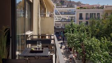 A balcony with a table and chairs, overlooking a street with pedestrians and buildings.