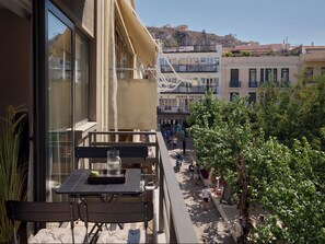 Un balcón con mesa y sillas, con vista a una calle con gente y edificios.