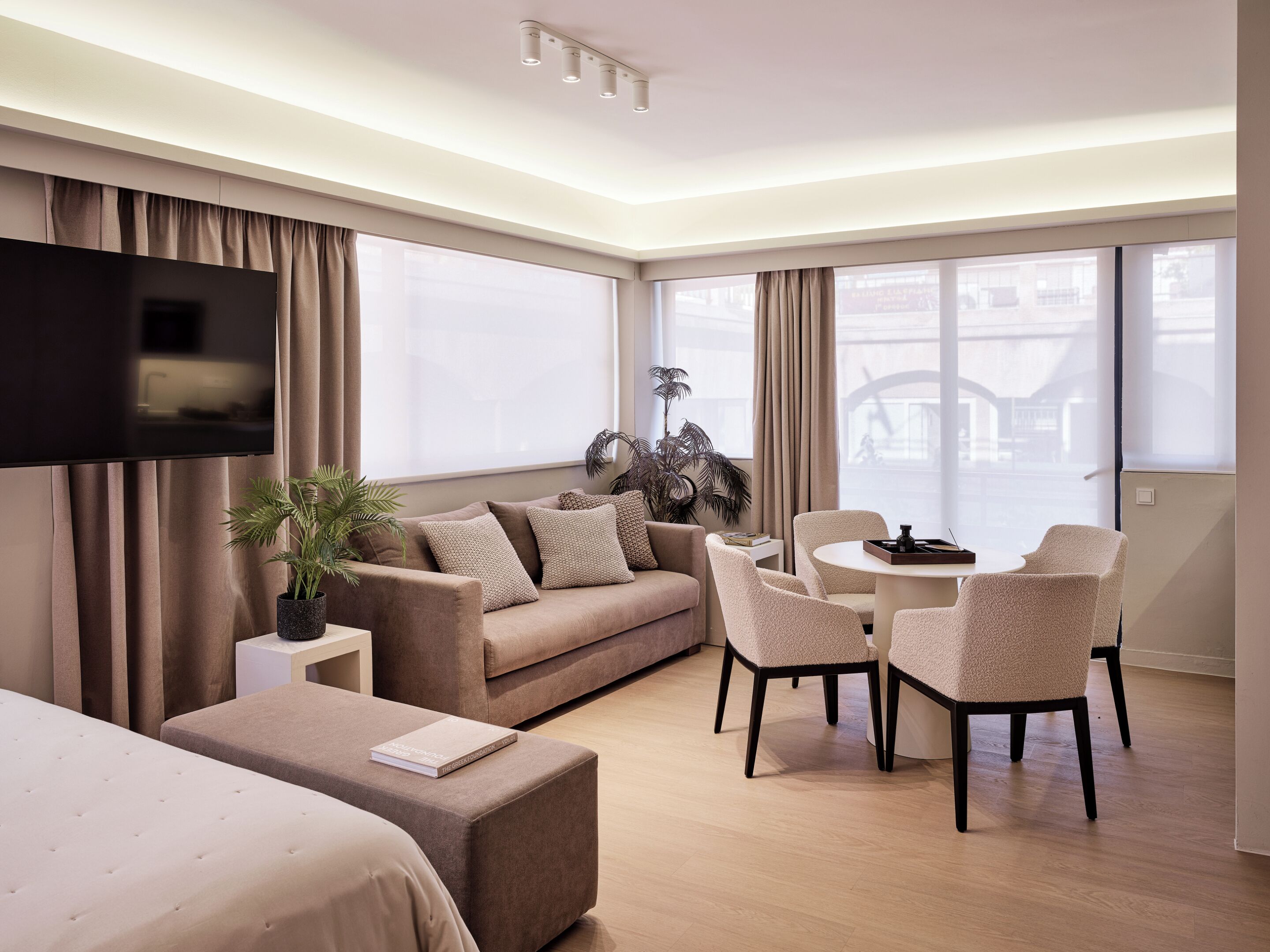 Quarto de hotel moderno com sofá, mesa de jantar, cadeiras, TV de tela plana e planta em vaso.