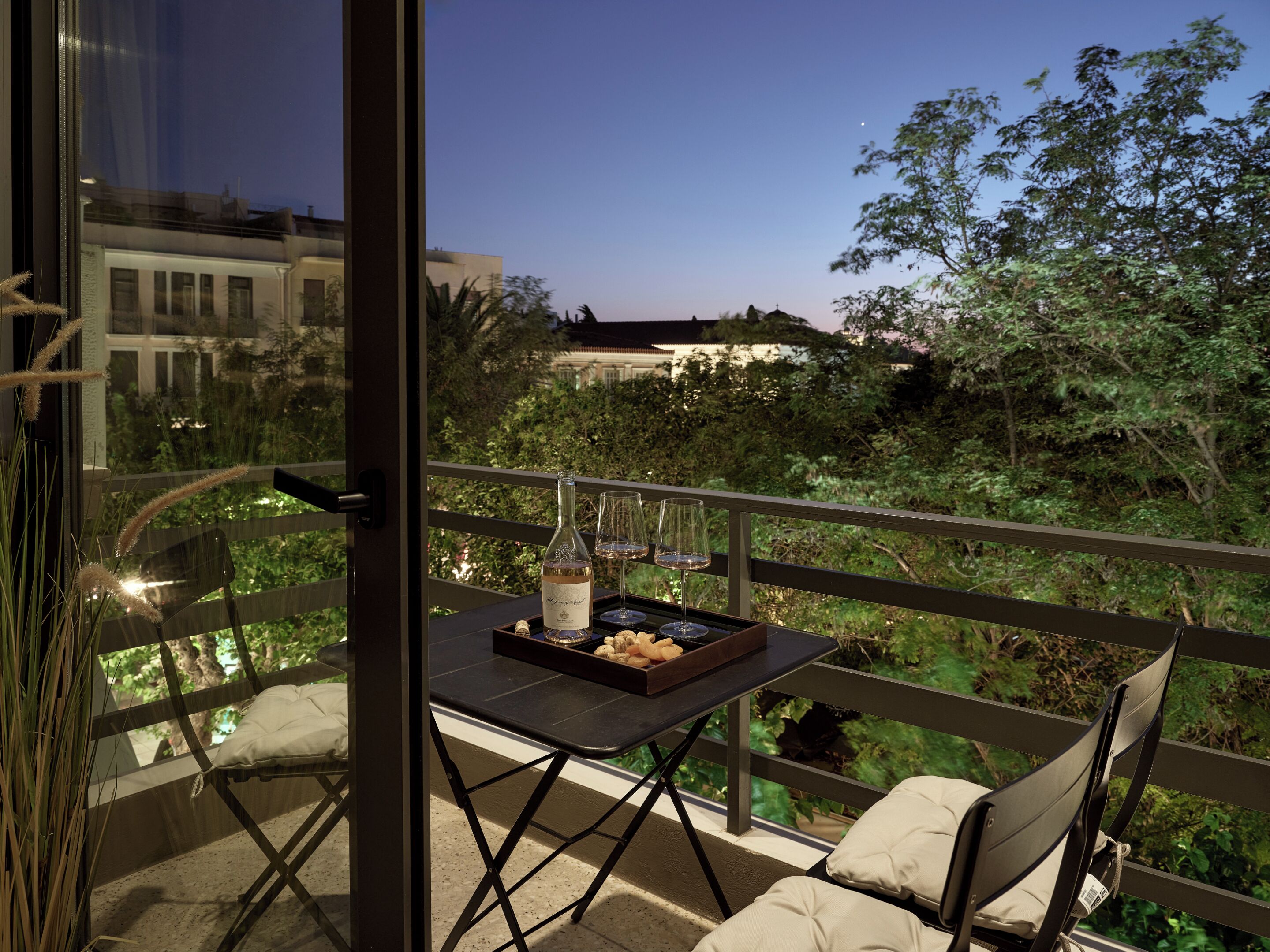 A balcony with a table set for two, a bottle of wine, and a tray of snacks.