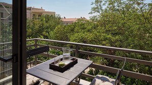 A balcony with a table, a chair, and a view of a building and trees. - Momo Suites Acropolis by Aura Homes (Athens)