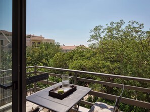 A balcony with a table, a chair, and a view of a building and trees. - Momo Suites Acropolis by Aura Homes (Athens)
