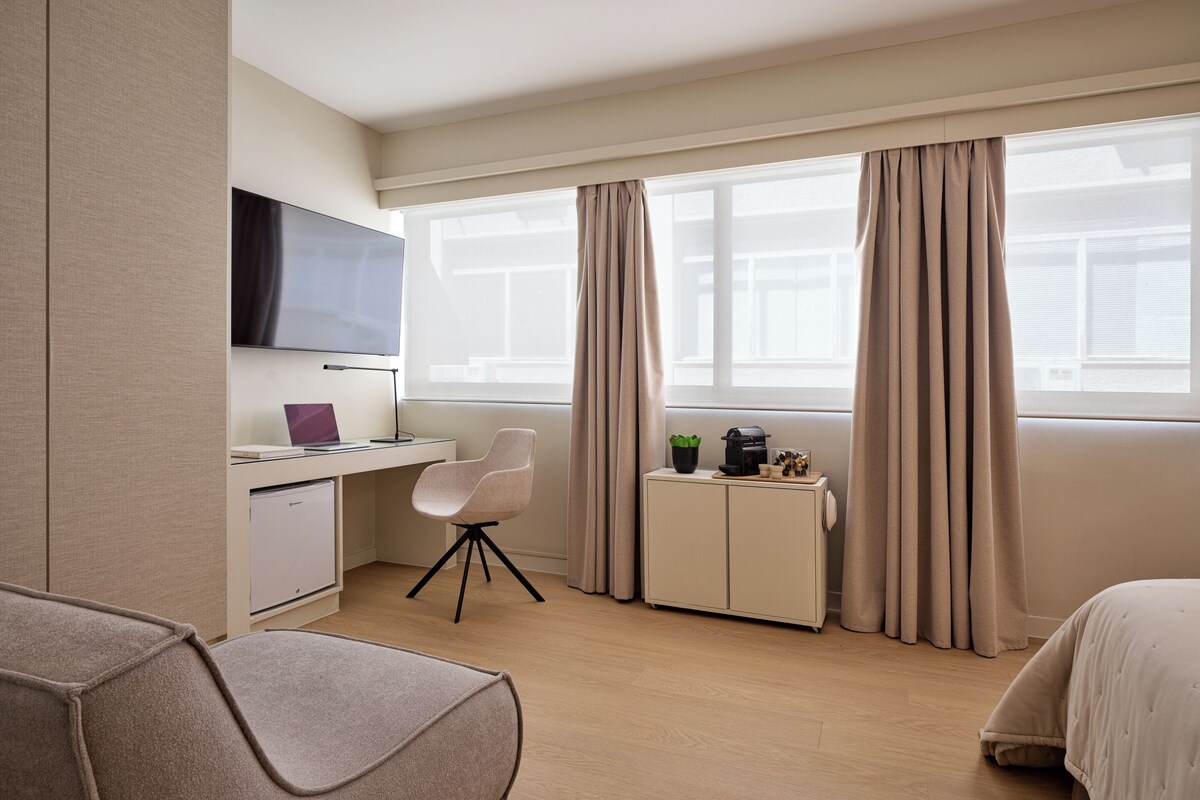 Una habitación de hotel con cama, escritorio con computadora, televisor y ventana con cortinas.