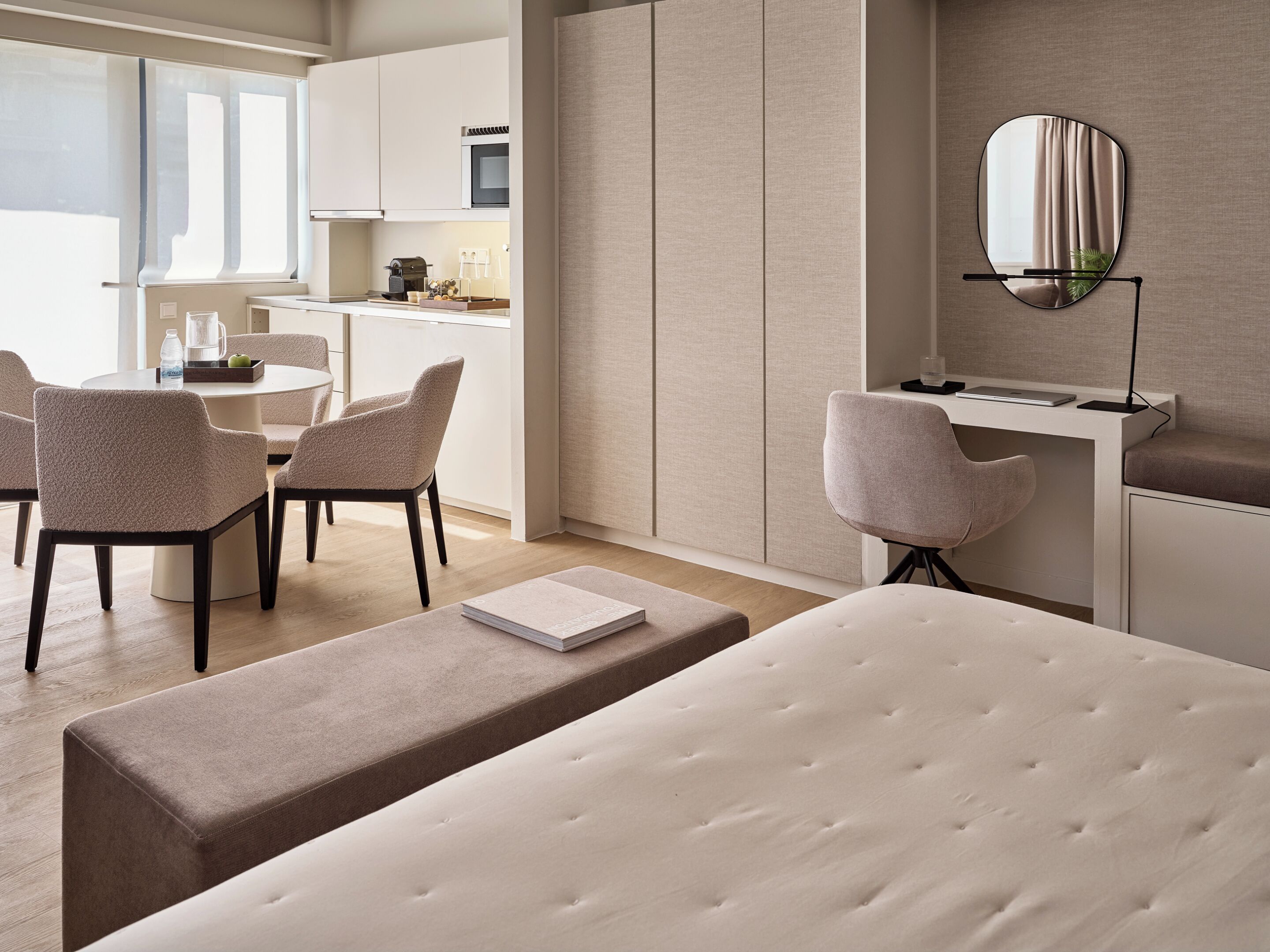 A modern hotel room with a bed, a desk, and a dining area.
