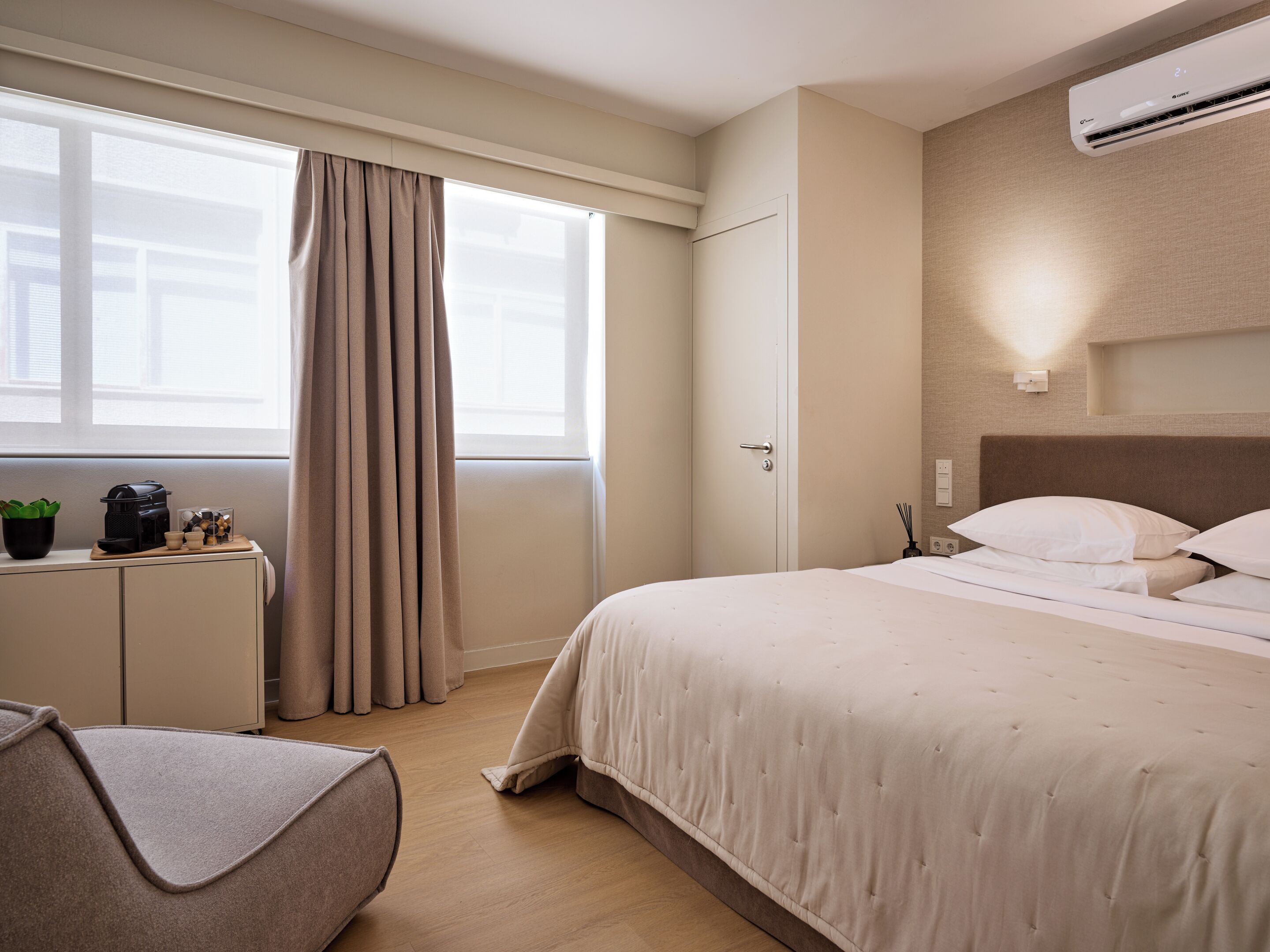A hotel room with a bed, a desk, a chair, and an air conditioning unit.