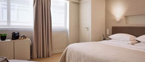 A hotel room with a bed, a desk, a chair, and an air conditioning unit.
