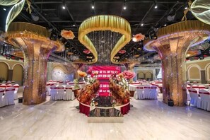 A banquet hall with a central stage, round tables, and decorative columns. - Wanshou Palace Hotel (Lanzhou)