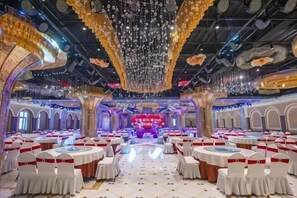 Un salón de banquetes con mesas redondas, manteles blancos y cintas rojas.