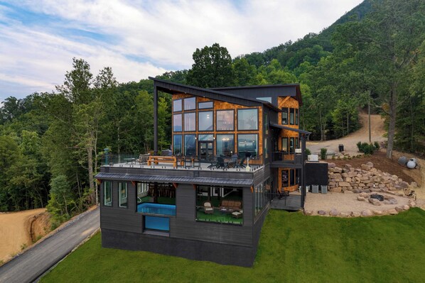 A modern two-story house with a large glass facade, a deck, and a swimming pool. - Skyline Sanctuary by Avantstay Indoor Pool, Game Room, Firepit, Mountain Views, Luxe Design (Sevierville)