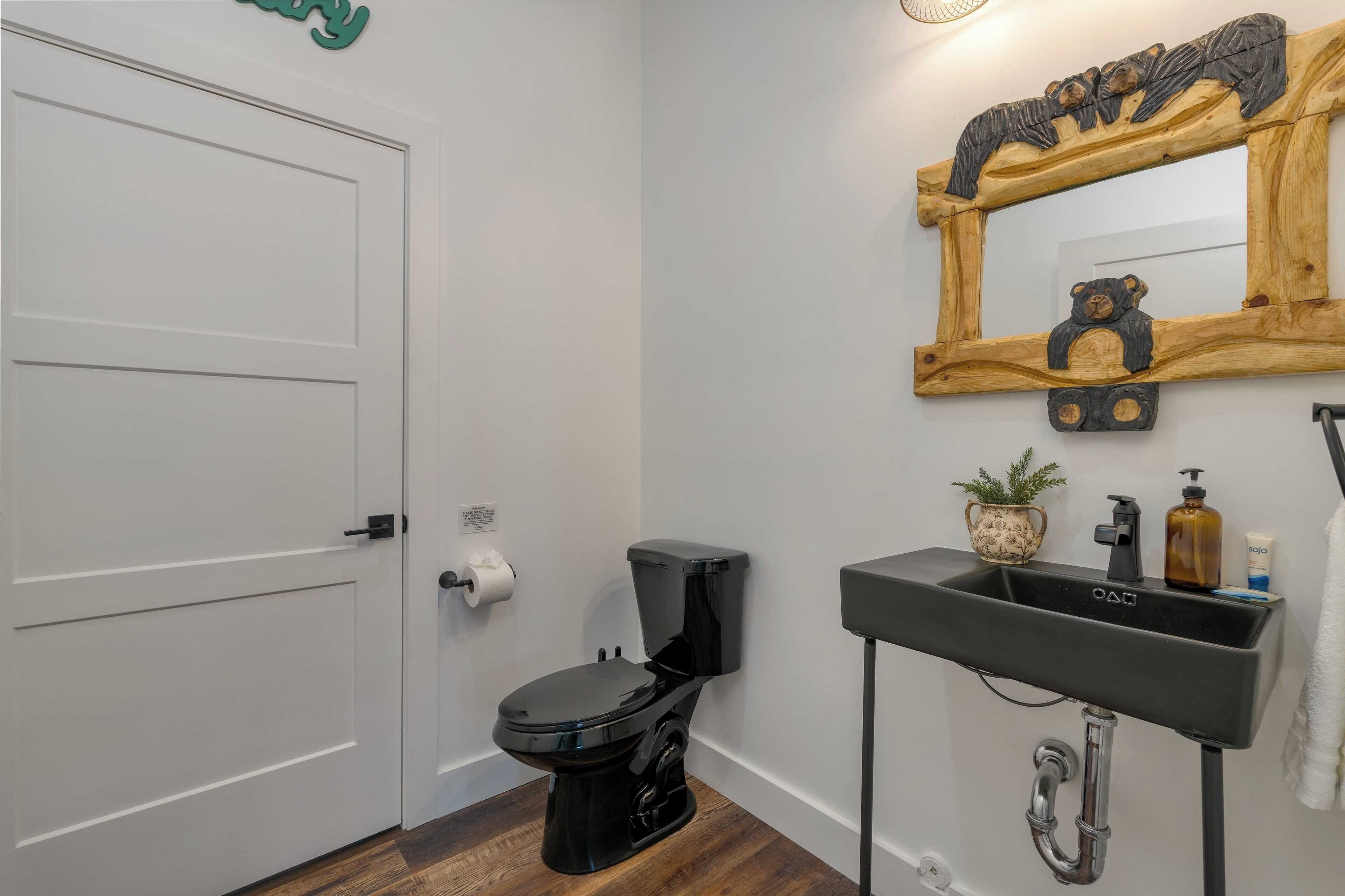 Une salle de bain avec une porte blanche, des toilettes noires, un miroir encadré en bois et un lavabo noir avec un robinet.