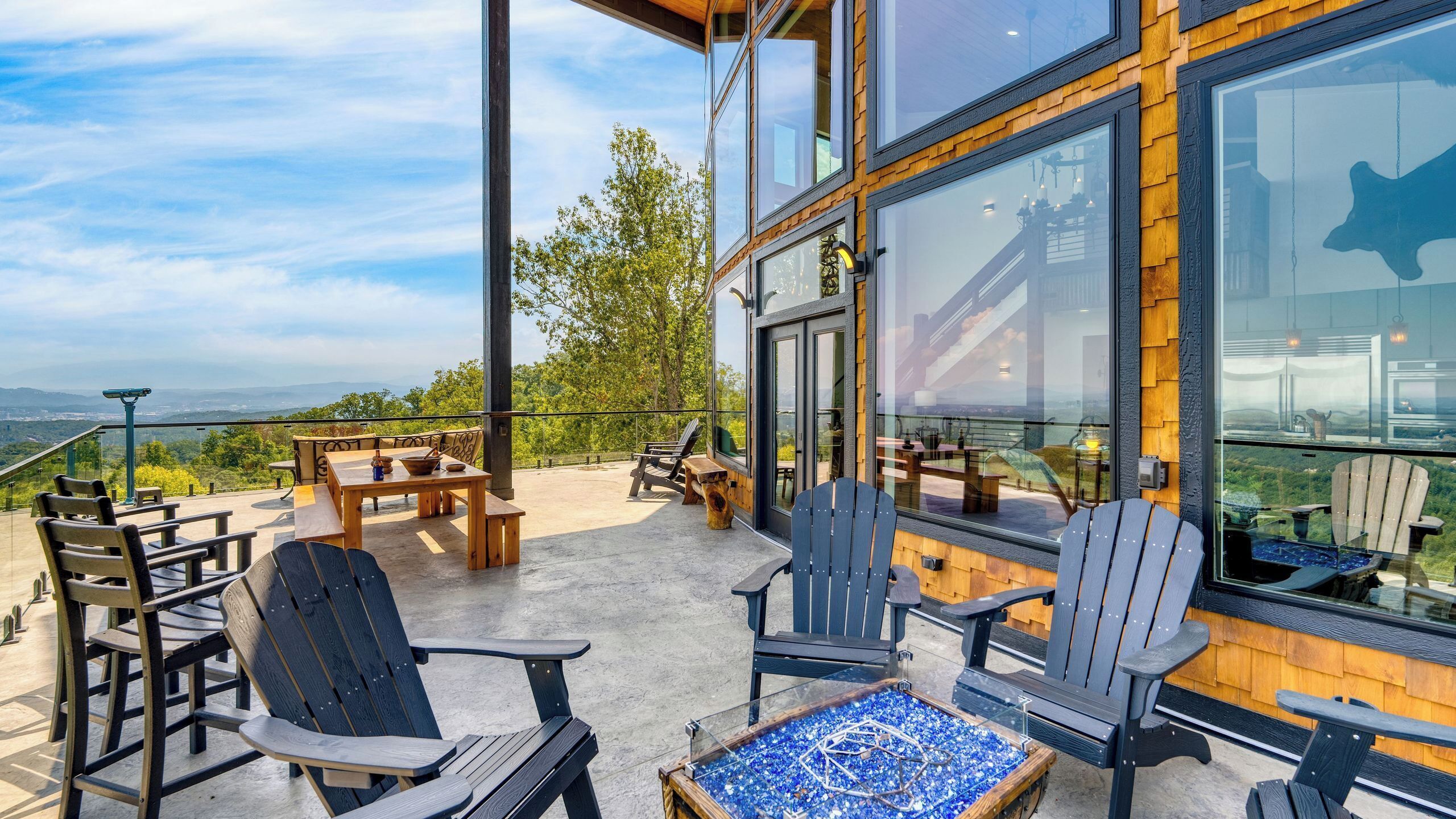 A modern outdoor seating area with Adirondack chairs and a glass-top table, overlooking a scenic landscape.