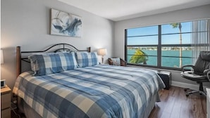 Un dormitorio con una cama grande, un escritorio, una silla y una ventana con vista al mar.