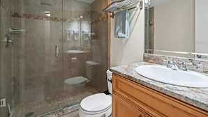 Un baño moderno con ducha de vidrio, lavabo blanco y muebles de madera.