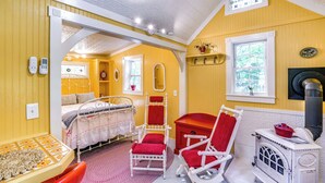 A cozy room with a bed, a red chair, a small table, and a white stove. - Studio w/ Trail Access ~ 10 Mi to Brattleboro! (Vernon)