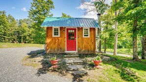 A small wooden cabin with a red door and a green roof, surrounded by trees and a gravel path. - Studio w/ Trail Access ~ 10 Mi to Brattleboro! (Vernon)