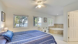 A bedroom with a bed, a ceiling fan, a window, a bathroom with a bathtub, and a door. - Lake Champlain Retreat w/ Grill, Fire Pit! (Chazy)