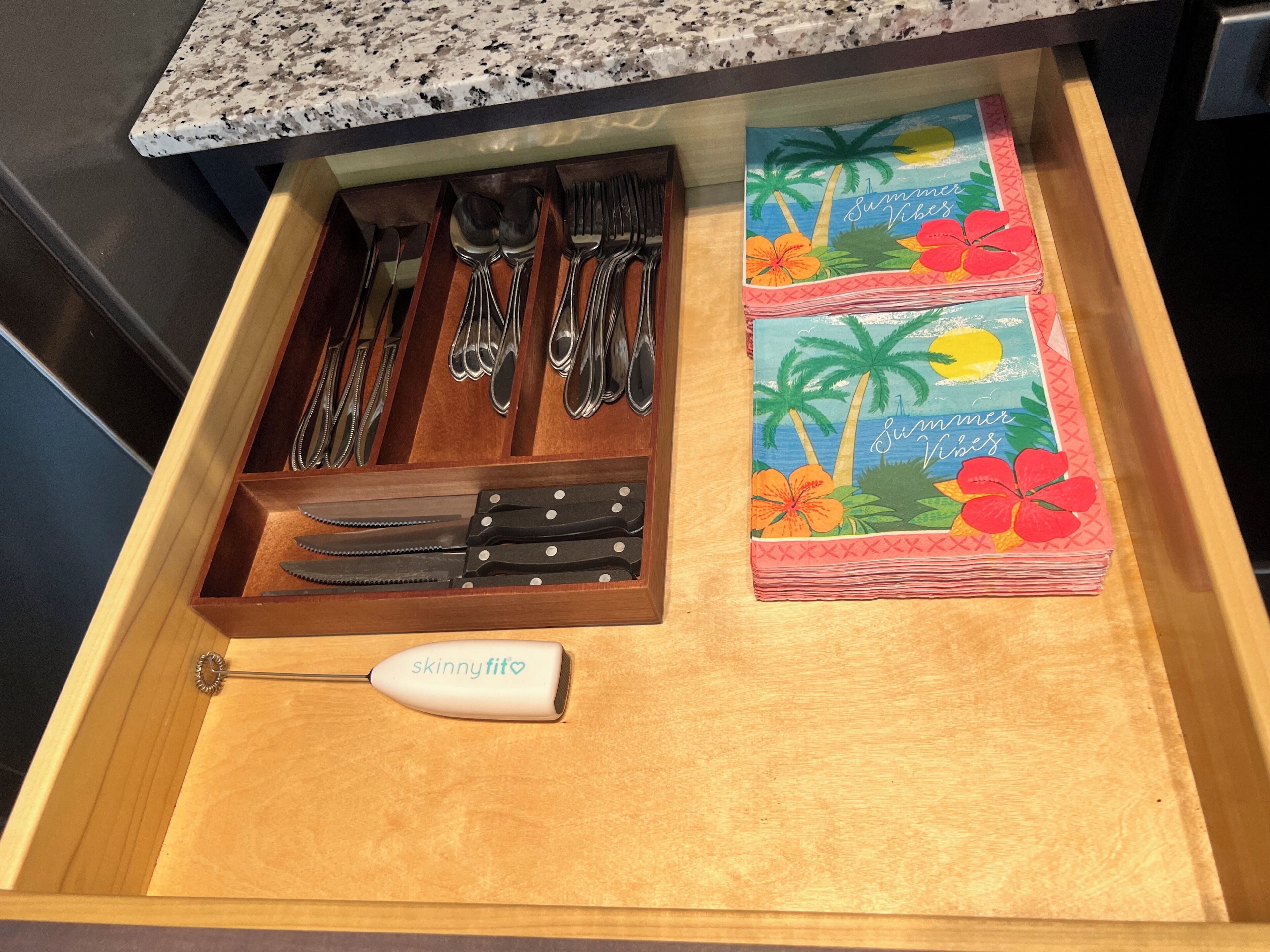 A drawer with utensils, a knife set, and a stack of cards with tropical designs.