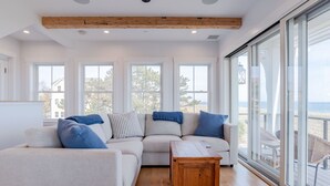 Una sala de estar moderna con un amplio sofá modular, una mesa de centro de madera y grandes ventanas con vista a la playa.
