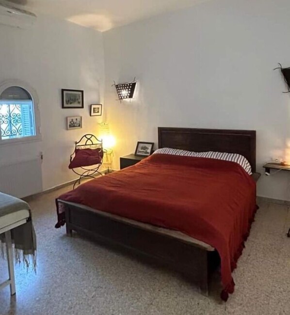Une chambre à coucher avec un lit, une chaise, une table de chevet, une lampe et une fenêtre.