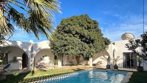 Una piscina con un árbol en el centro, rodeada por un edificio blanco con arcos y una antena parabólica.