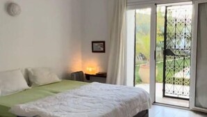 Un dormitorio con cama, mesita de noche, ventana con cortinas y vistas al exterior.