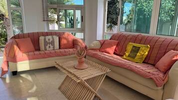 A living room with a beige sectional sofa, a small wooden coffee table, and large windows with views of greenery.
