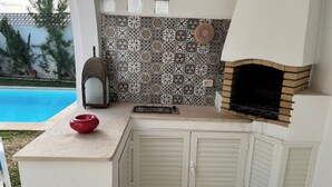 Una cocina al aire libre compacta con una parrilla integrada, una olla roja y un salpicadero con diseño.