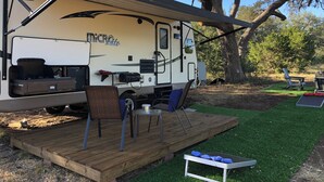 A recreational vehicle with a covered deck area, a grill, and a small table with chairs. - Ramblin' Rose: a sweet Glamper for 2 under the stars in Dripping Springs (Dripping Springs)