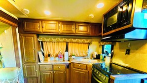 A compact kitchen with wooden cabinets, a stove, a microwave, and a sink. - Ramblin' Rose: a sweet Glamper for 2 under the stars in Dripping Springs (Dripping Springs)