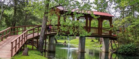 A wooden bridge over a calm river, surrounded by lush greenery and trees.