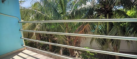 Un balcón con barandillas metálicas, una pared azul y palmeras al fondo.