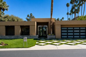 A modern two-story house with a garage, a well-maintained lawn, and palm trees in the background.