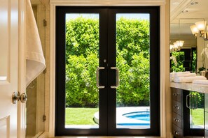 A double door leading to a pool area with a view of a lush green garden.