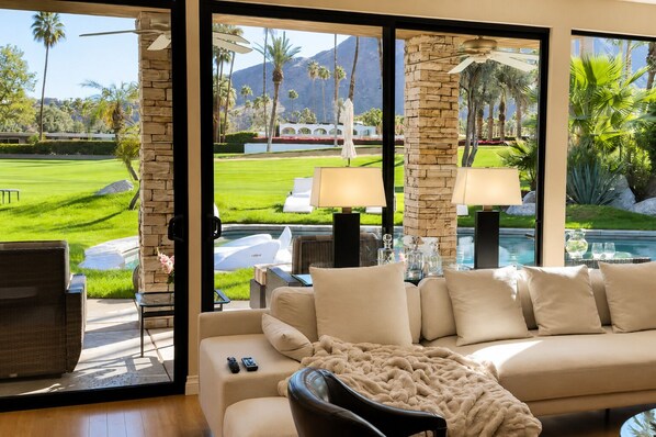 A modern living room with a large window overlooking a pool and a well-manicured lawn.