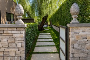 A stone pathway leading to a building with a modern design, flanked by neatly trimmed hedges and decorative urns. - NEW LISTING - PALM SPRINGS INDIAN CANYONS LUXURY ESTATE WITH GOLF COURSE VIEWS (Palm Springs)