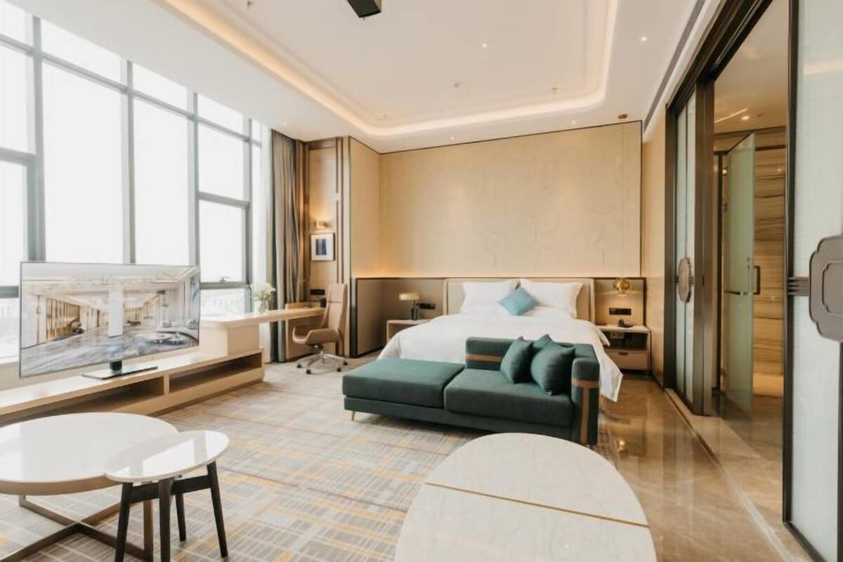 Ein modernes Hotelzimmer mit einem großen Bett, einer Couch, einem Schreibtisch und einem Fernseher.