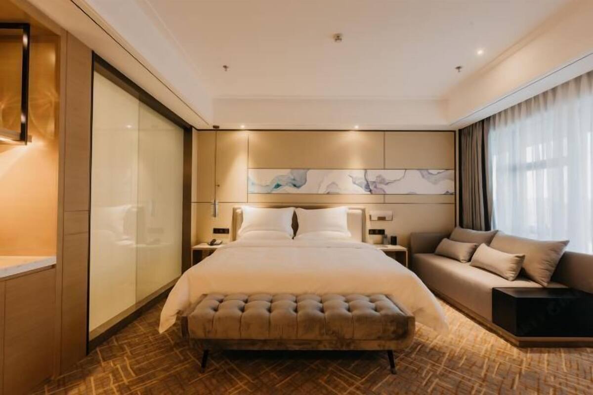 Ein Hotelzimmer mit einem großen Bett, einer Couch, Holzboden und einer Wand mit abstrakter Kunst.