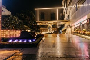 A nighttime view of a building with a fountain, illuminated walkway, and arched windows. - Jinquan Yujing Hotel (Enping)