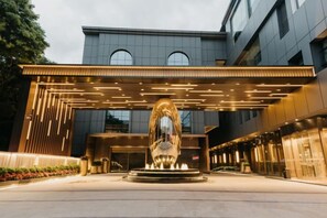 A modern building with a central fountain, a covered entrance, and a well-lit facade. - Jinquan Yujing Hotel (Enping)