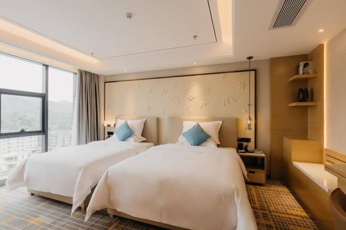 Ein Hotelzimmer mit zwei Betten, einem großen Fenster, einem Nachttisch und einer eingebauten Bank.