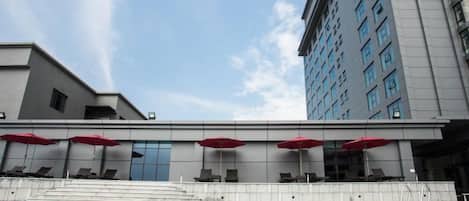 Ein modernes Hotel mit Schwimmbad, roten Sonnenschirmen und einer Treppe zum Poolbereich.