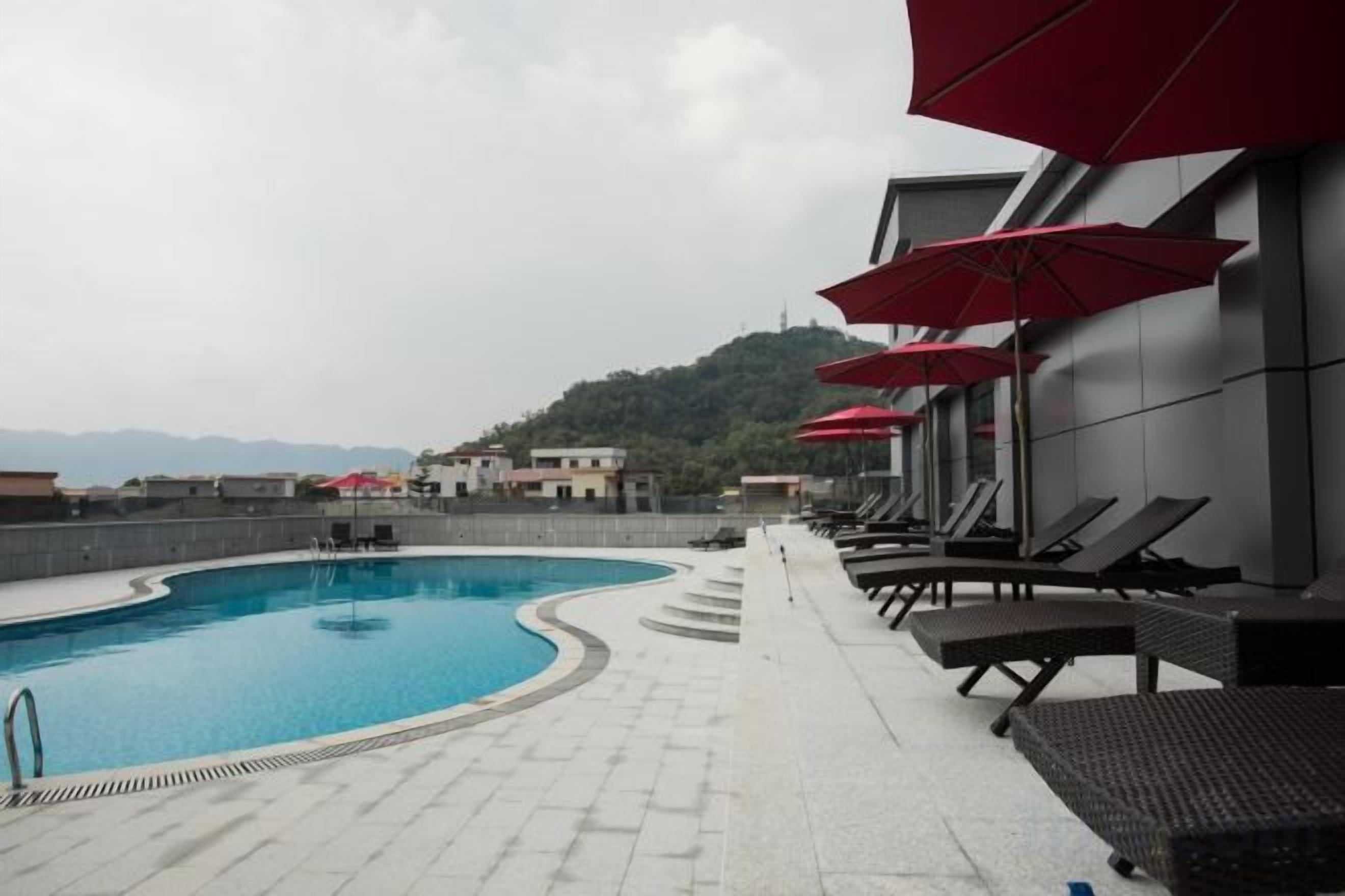 Une piscine avec des chaises longues et des parasols, un escalier menant à une terrasse, et une vue sur des collines en arrière-plan.