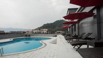 Una piscina con sillones de descanso y sombrillas, una escalera que conduce a una terraza y vistas de colinas al fondo.